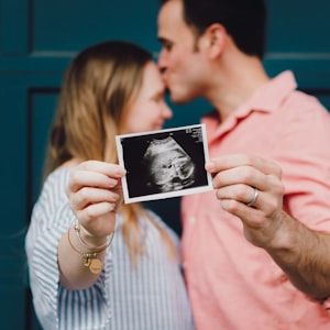 Couple kissing while holding their gender reveal scan